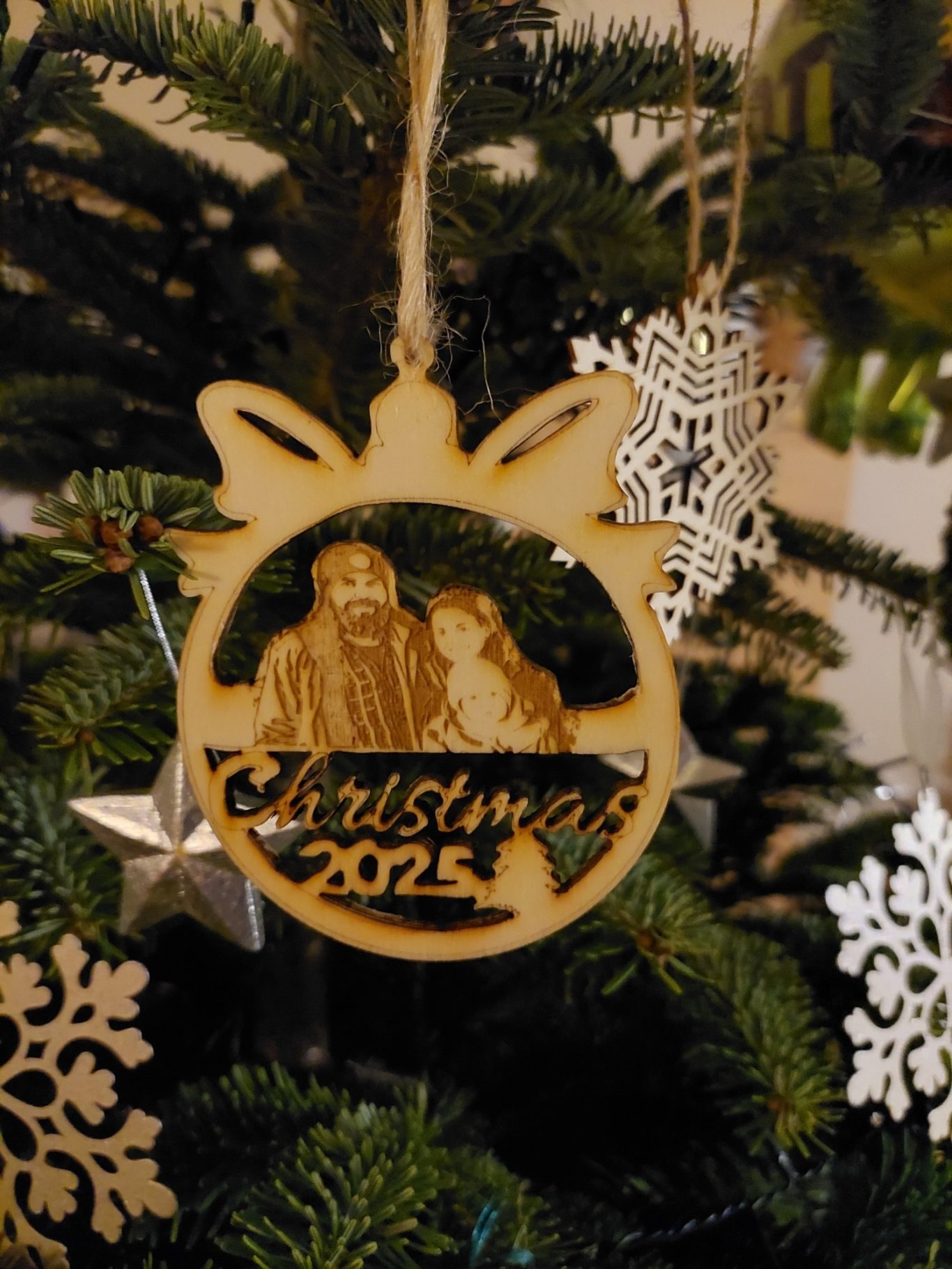 Holzornament / Baumschmuck für Weihnachten 2025 mit personalisiertem Bild Holzornament mit der Aufschrift "Christmas 2025" und einer Familie, an einem Weihnachtsbaum hängend.
