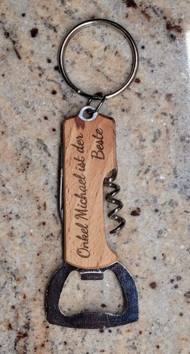 Schlüsselanhänger-Multitool mit Flaschenöffner und Messer Ein Flaschenöffner mit Schlüsselring, aus Holz und Metall, graviert mit Text.