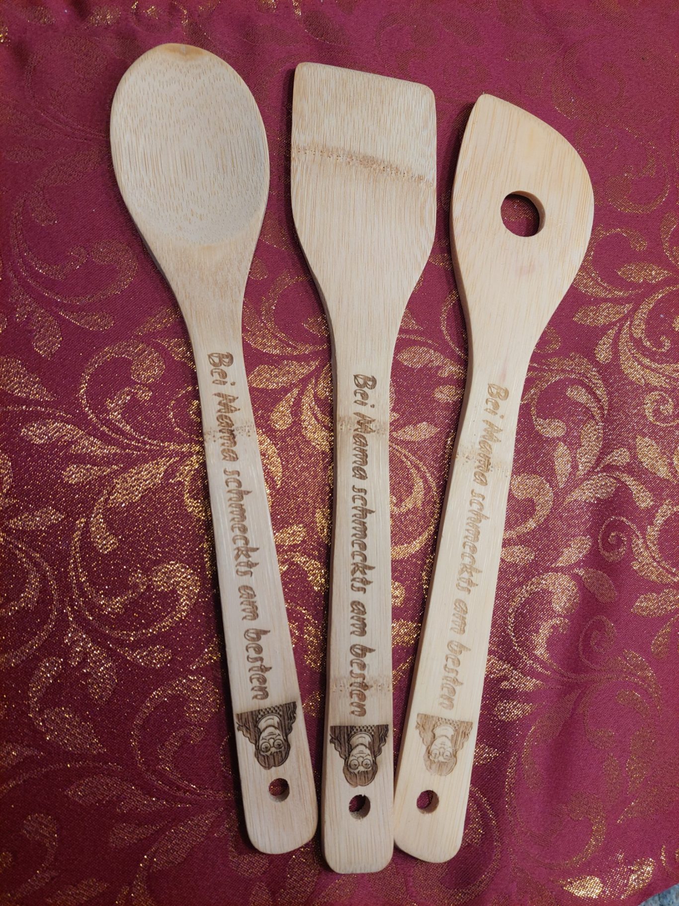 Drei Holzkochlöffel mit individueller Gravur und Bild Drei Holzkochlöffel mit Gravuren, auf rotem Tischläufer angeordnet.