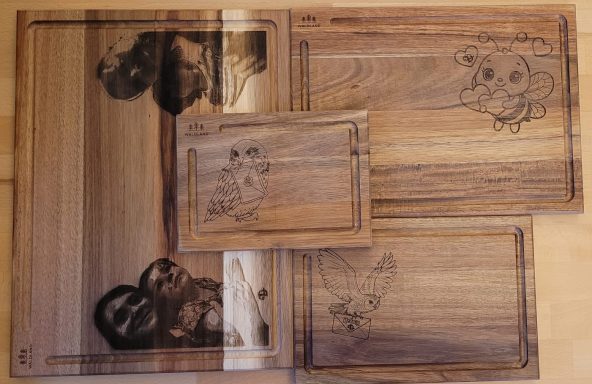 Set aus 4 verschieden großen Schneidebrettern aus Holz mit individuellen Gravuren Eine Anordnung von Holz-Tabletts mit gravierten Mustern und Figuren.